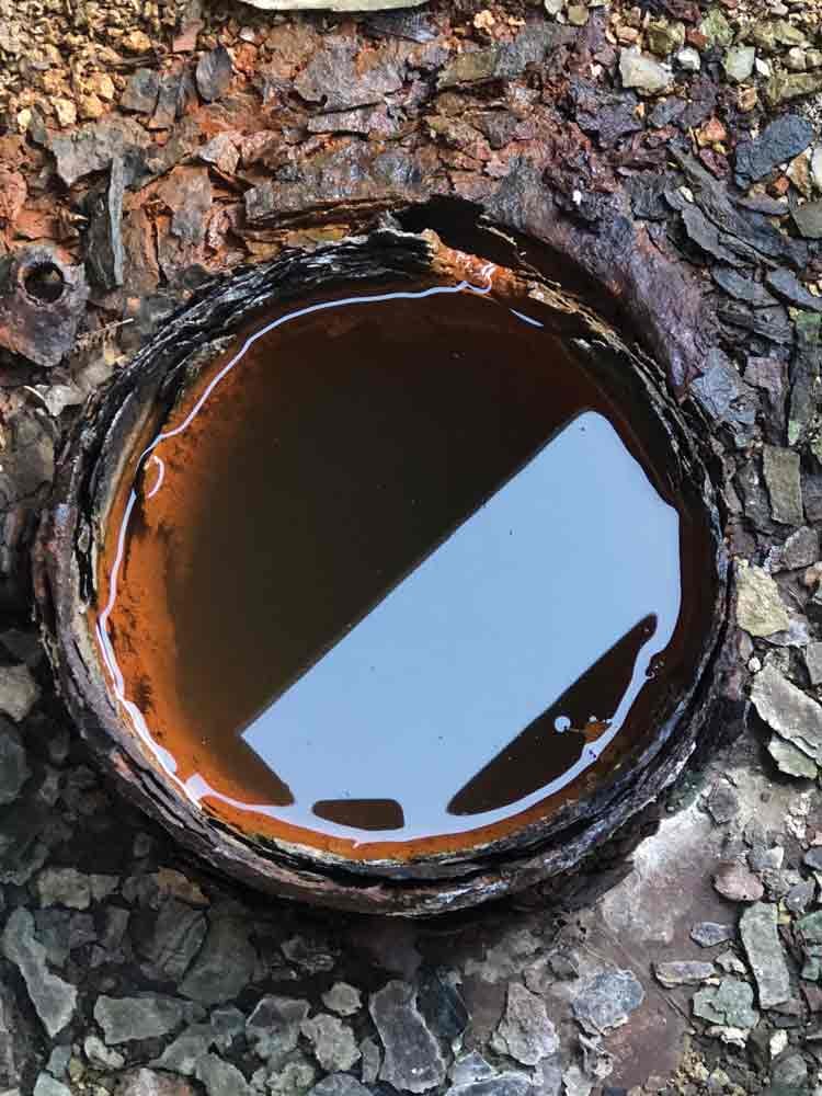 A broken pipe filled with rusty, stagnant water surrounded by cracked and peeling paint.