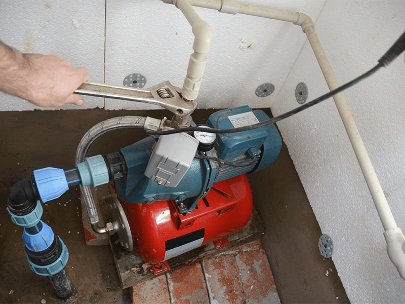 A person's hand uses a wrench to adjust a fitting on a water pump system.