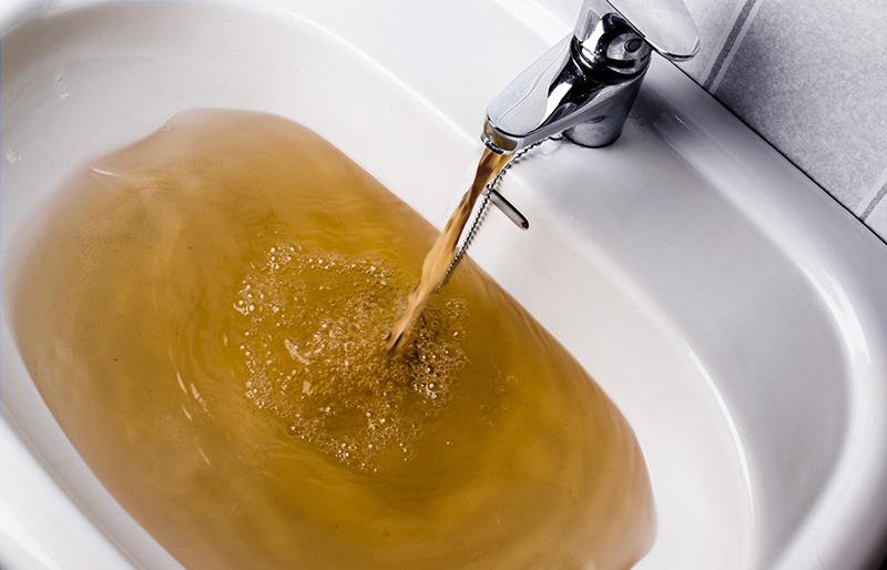 Brown, murky water pouring from faucet into white sink